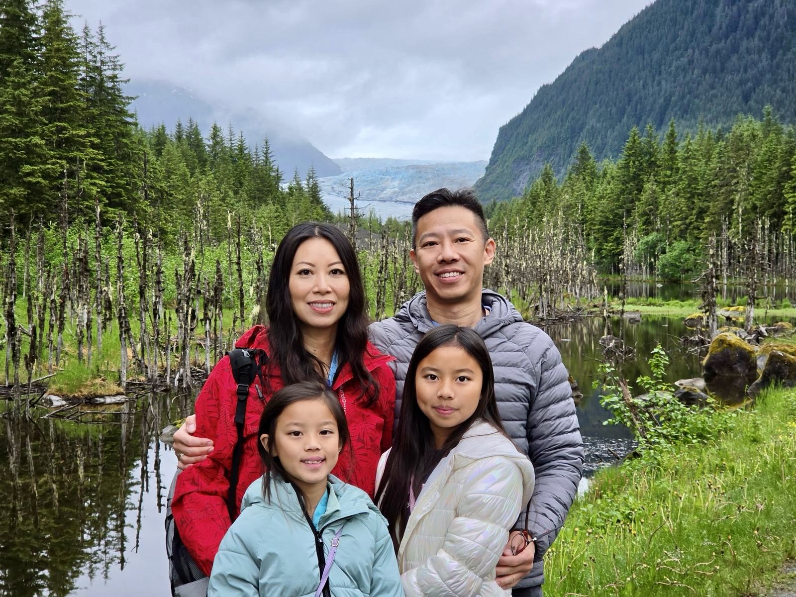 The Huang family together beside a still lake, with a glacier and forested mountains behind them.